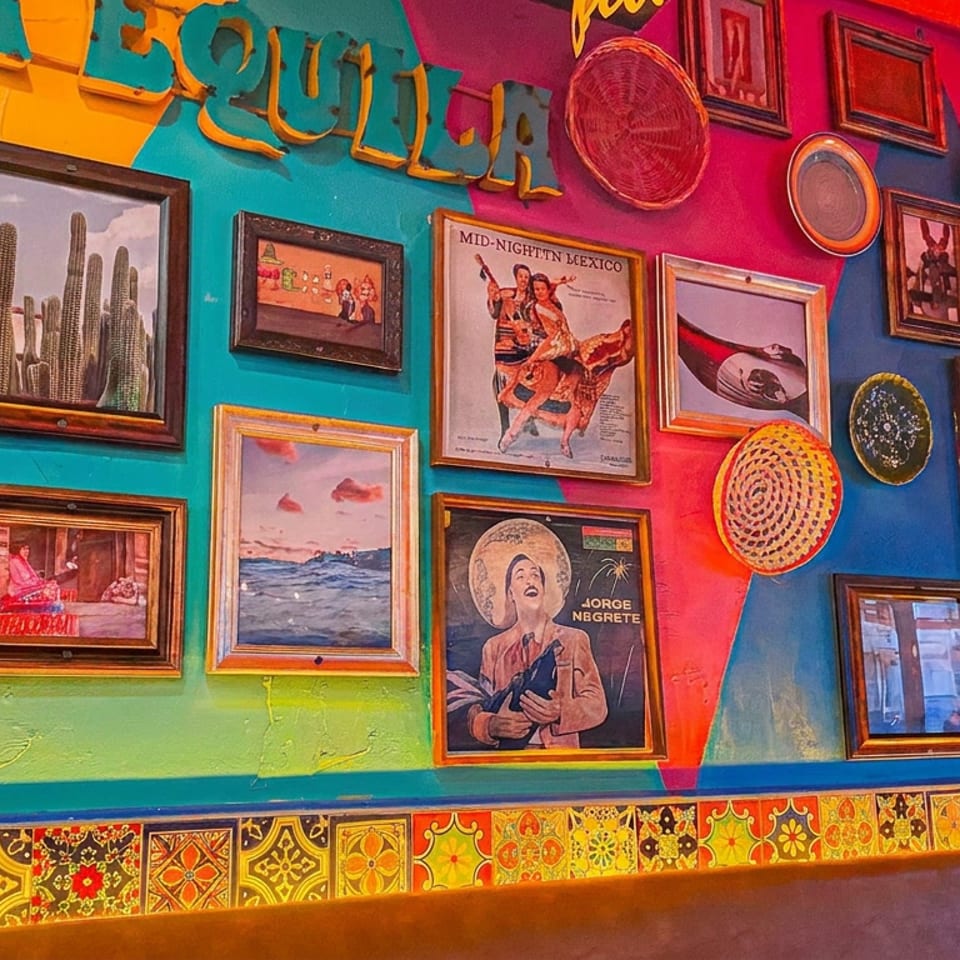 Colorful Mexican-inspired wall displays framed artwork, decorative plates, flowers, and a patterned tile border.