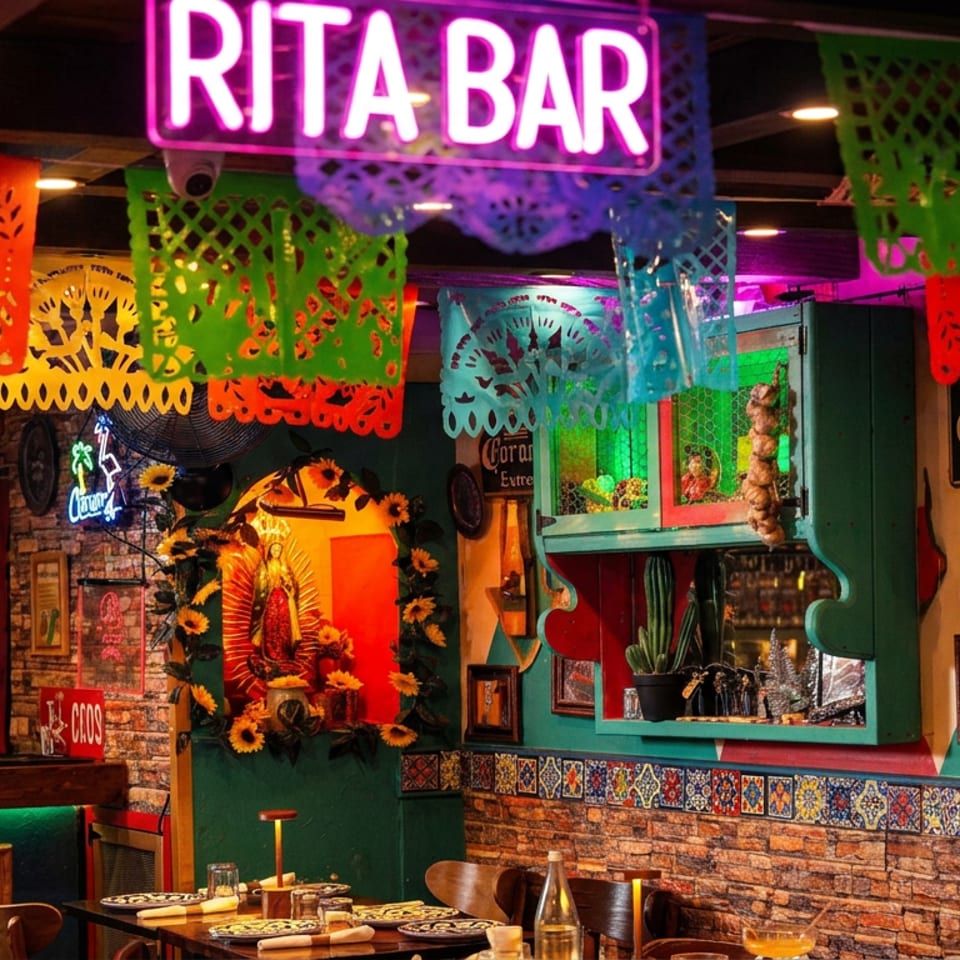 Colorful Mexican restaurant bar decorated with papel picado banners, a Rita Bar sign, Corona branding, and festive religious artwork.
